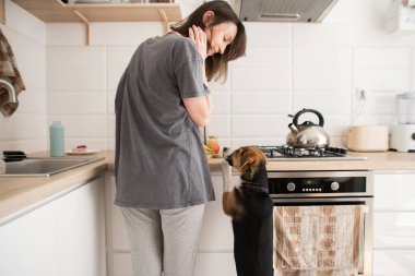 Genç bir kadın mutfakta köpekle yemek pişiriyor.