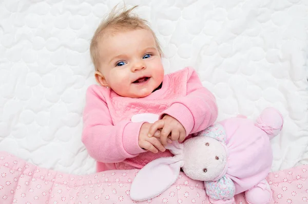Bayi perempuan yang bahagia tersenyum di tempat tidur dengan kelinci mainannya — Stok Foto