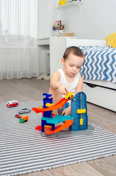 Menino de cinco anos jogando carros de brinquedo e uma estrada — Fotografia de Stock