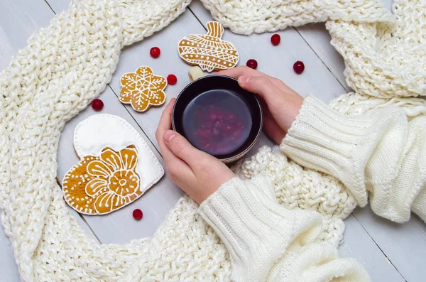 Mains dans un pull tenant une tasse de thé et un cookie sur un bois — Photo