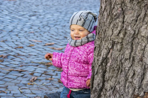 Portrait d'une petite fille qui regarde par derrière un arbre au — Photo