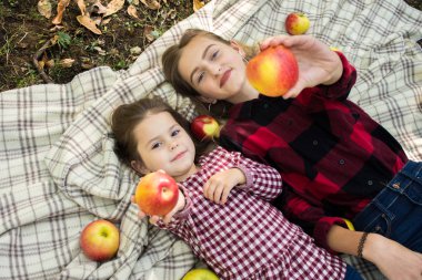 Ekose elbiseli iki kız kardeş elma yer.