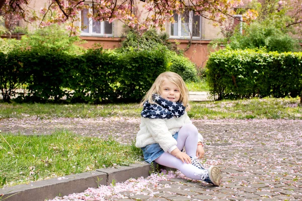 一个金发碧眼的小女孩与落下来的樱花花瓣玩耍的画像 — 图库照片