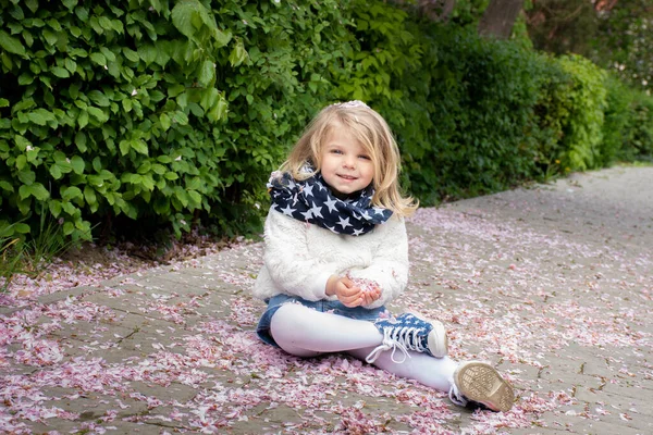 一个金发碧眼的小女孩与落下来的樱花花瓣玩耍的画像 — 图库照片