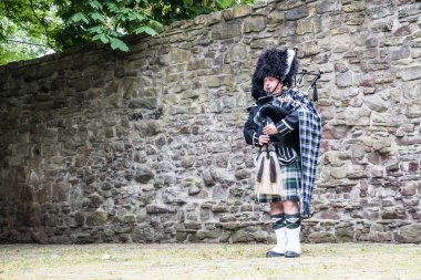 Traditional scottish bagpiper in front of historic wall clipart
