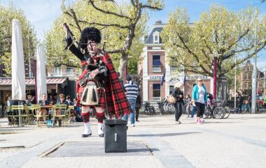 Amsterdam , Netherlands - April 31, 2017 : Scottish bagpiper tuning his instrument in the streets of Amsterdam wearing his Royal Stuart tartan clipart