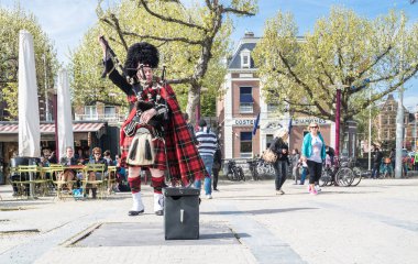 Amsterdam , Netherlands - April 31, 2017 : Scottish bagpiper tuning his instrument in the streets of Amsterdam wearing his Royal Stuart tartan clipart