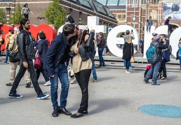 Amsterdam, Holandia - 31 kwietnia 2017 r.: Para biorąc selfie, podczas gdy ludzie chodzą I Amsterdam liter na placu przed Muzeum, upływ czasu — Zdjęcie stockowe