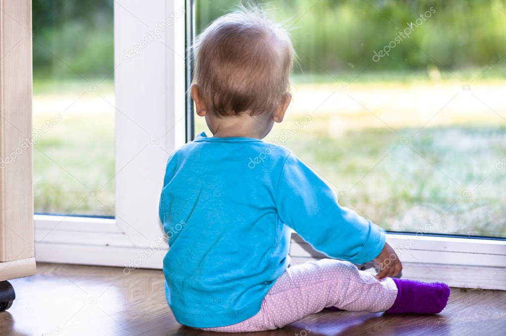 View form behind of toddler sitting in front of a big window