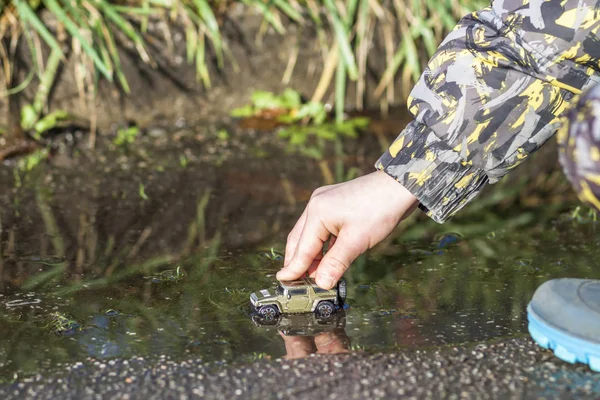 Liten pojke i färgade gummi stövlar leker med sin leksaksbil i pöl — Stockfoto