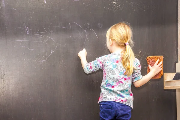 Cute little girl writing on chalkboard — Stock Photo, Image