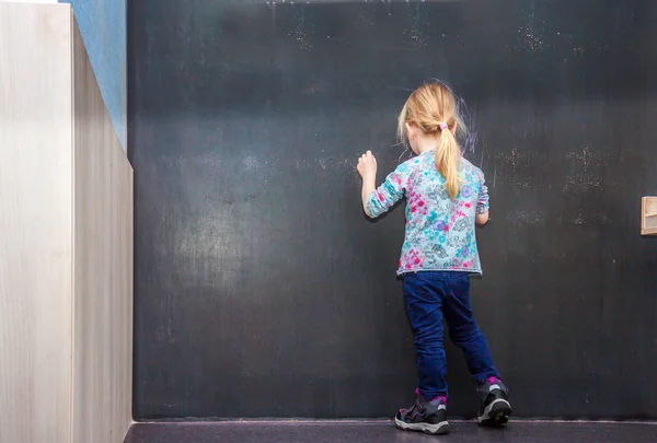 Cute little girl writing on empty chalkboard — Stock Photo, Image