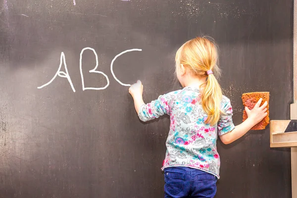 Cute little girl writing ABC on chalkboard — Stock Photo, Image