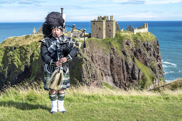 Traditional scottish bagpiper in full dress code at Dunnottar Castle in Stonehaven