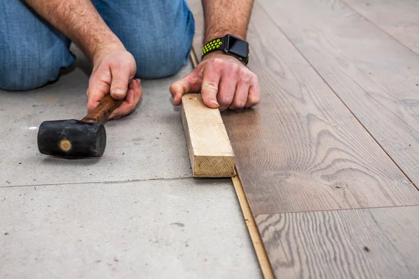 Man laying laminate by using hammer and wooden block — Stock Photo, Image
