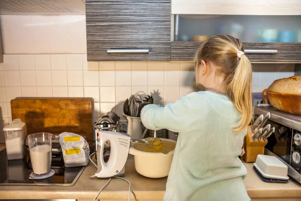 Маленька дівчинка випікає вафлі на кухні після рецепту на смартфоні — стокове фото