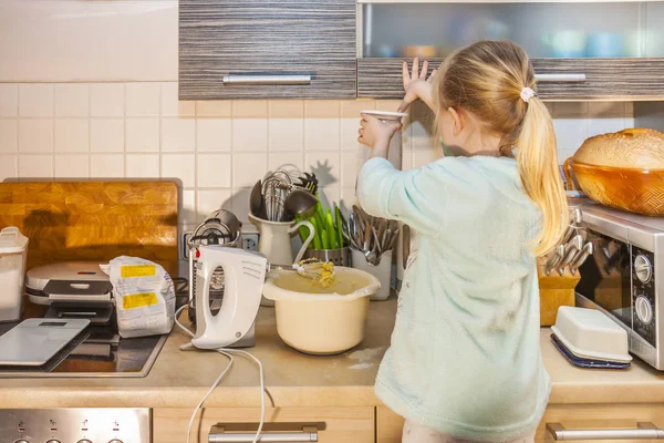 Маленька дівчинка випікає вафлі на кухні після рецепту на смартфоні — стокове фото