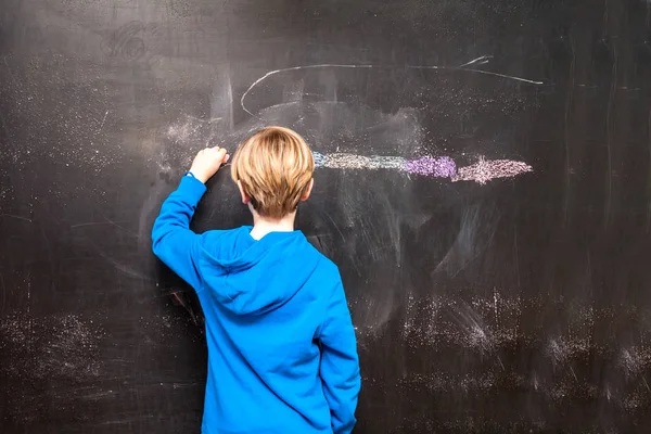 Back view of a little boy painting something on a chalkboard — Stock Photo, Image