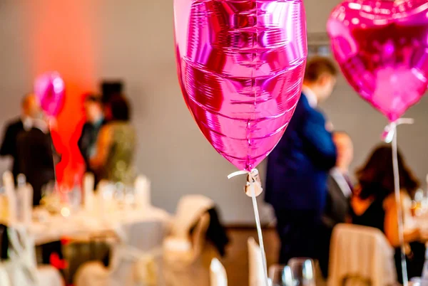 Pink festive balloons shape of heart with the party guests in the background