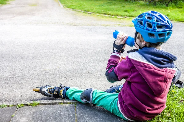 Malý chlapec na sobě kolečkové brusle sedí a jíst a pít minerální vody — Stock fotografie