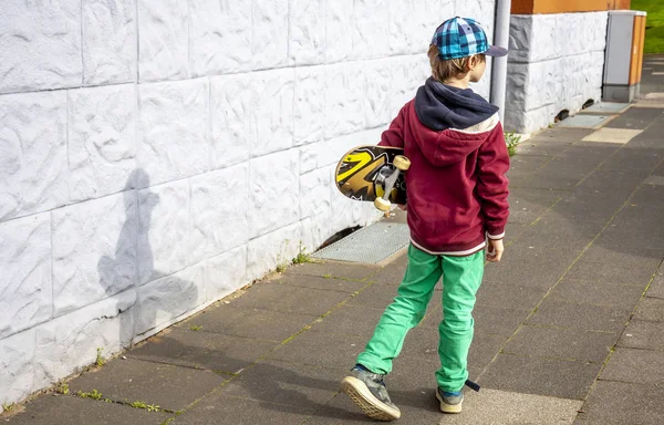Ung promenader längs vit vägg med longboard — Stockfoto