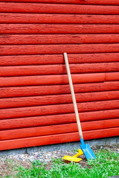 Pelle à jouet et bêche debout à côté du mur en bois rouge — Photo