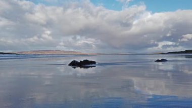 Bulutlar ıslak kumlu sahile yansıyor.