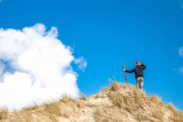 Jeune garçon avec un bâton debout sur le dessus de la dune de sable — Photo