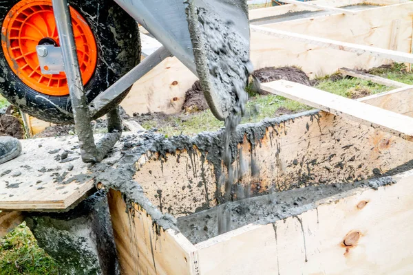 Pouring concrete into wooden frame with wheel barrow — Stock Photo, Image