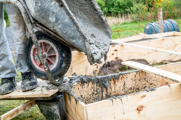 Pouring concrete into wooden frame with wheel barrow — Stock Photo, Image