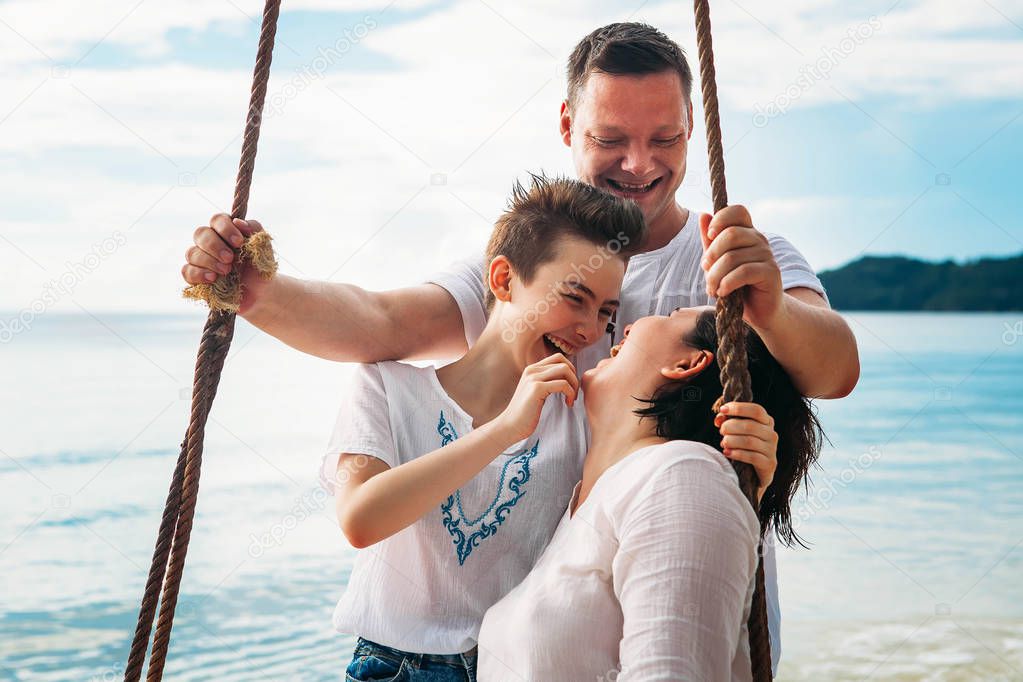 Family laughing siting on Swing tropical beach