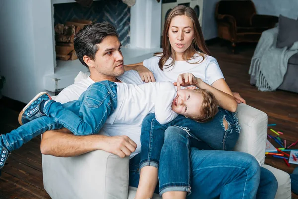 Padre y madre tumbados en el sofá y jugando con dos hijos pequeños —  Fotos de Stock