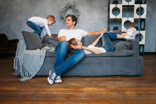 Father and mother lying on the sofa and playing with two little sons — Stock Photo, Image