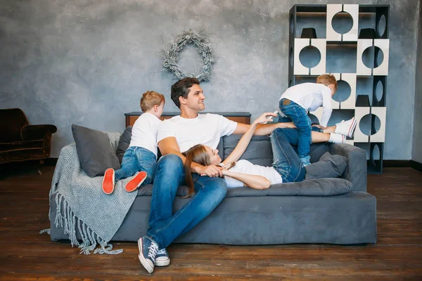 Father and mother lying on the sofa and playing with two little sons — Stock Photo, Image