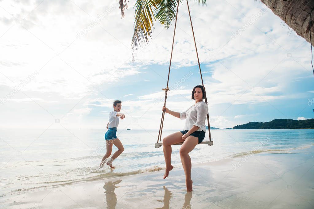 Happy woman on a swing tropical island while daughter is running next to her