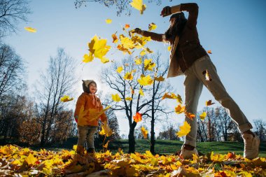 Anne kızı sonbahar yaprakları parkta atar.