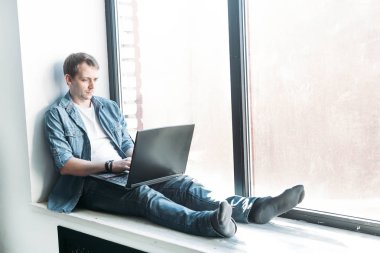 Yakışıklı hippi modern erkek tasarımcı evde dizüstü bilgisayar kullanarak çalışıyor.