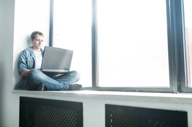 Yakışıklı hippi modern erkek tasarımcı evde dizüstü bilgisayar kullanarak çalışıyor.