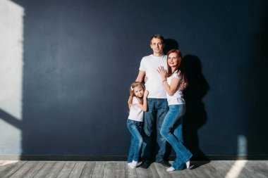 Mutlu aile portresi ayakta gri arka plan ahşap zemin oda pencere güneşli