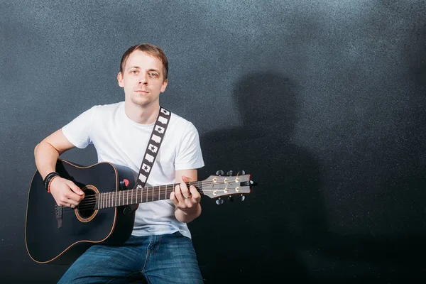 Neşeli gitarist. Gitar çalmak ve koltuğa otururken gülümseyen neşeli yakışıklı genç adam