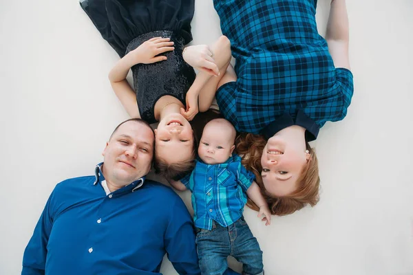 Feliz familia madre padre hija hijo retrato acostado en blanco piso habitación estudio azul —  Fotos de Stock