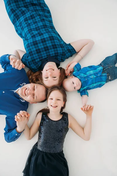 Feliz família mãe pai filha filho retrato deitado no chão branco quarto estúdio azul — Fotografia de Stock