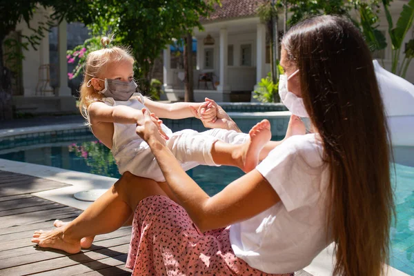 Mom and little daughter in protective masks near swimming pool