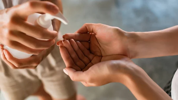 woman disinfecting with sanitizer hands to her friend