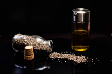 Siyah arka planda cam kavanozlardaki chia tohumları ve yağın yakın plan görüntüsü