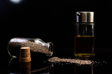 Siyah arka planda cam kavanozlardaki chia tohumları ve yağın yakın plan görüntüsü