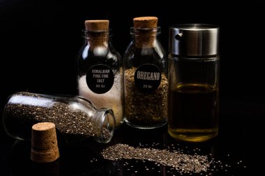 Farklı tohumların, baharatların ve yağın siyah arka plandaki kavanozlarda yakın plan görüntüsü