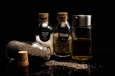 Farklı tohumların, baharatların ve yağın siyah arka plandaki kavanozlarda yakın plan görüntüsü