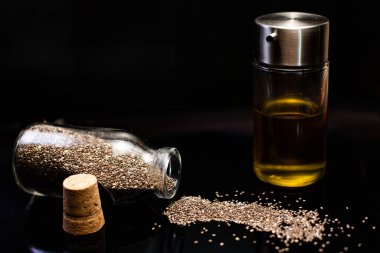 Siyah arka planda cam kavanozlardaki sağlıklı chia tohumları ve yağın yakın plan görüntüsü