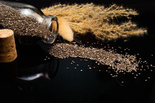 stock image close-up view of dry chia seeds and glass jar on black background